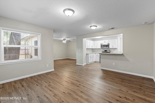 unfurnished living room with visible vents, baseboards, wood finished floors, a textured ceiling, and a ceiling fan