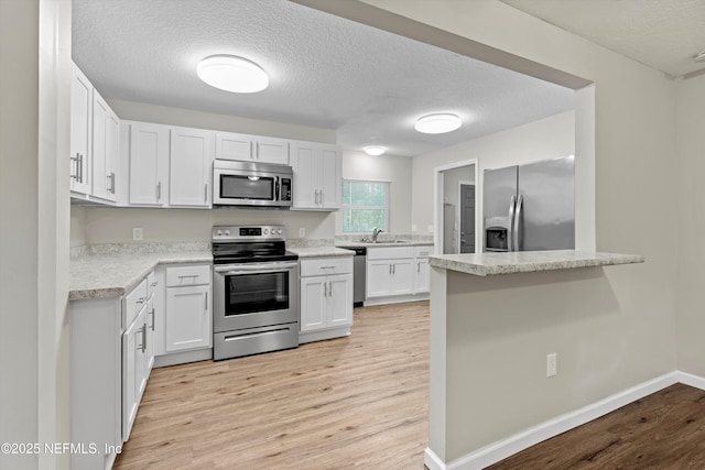 kitchen with stainless steel appliances, light wood-style floors, white cabinets, and light countertops