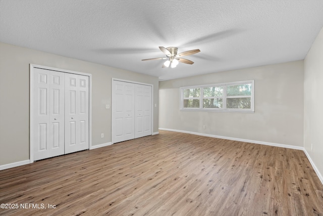 unfurnished bedroom featuring a textured ceiling, baseboards, multiple closets, and wood finished floors