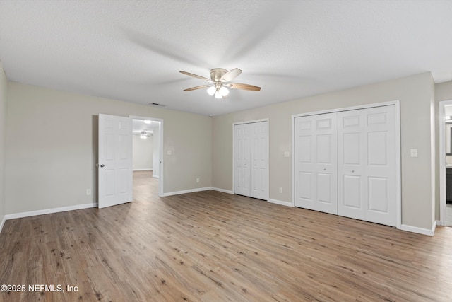 unfurnished bedroom featuring visible vents, baseboards, light wood finished floors, a textured ceiling, and two closets