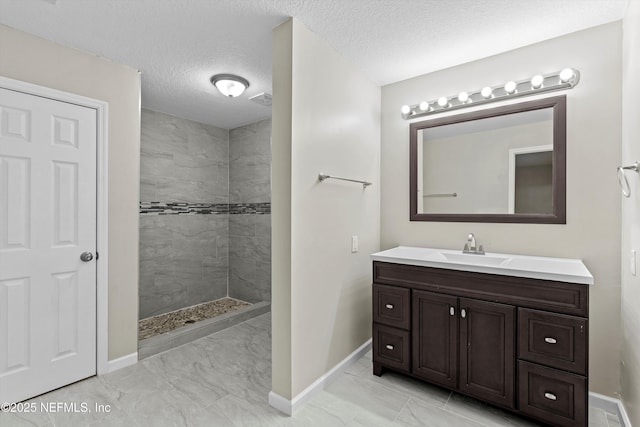 bathroom with vanity, a textured ceiling, marble finish floor, and tiled shower