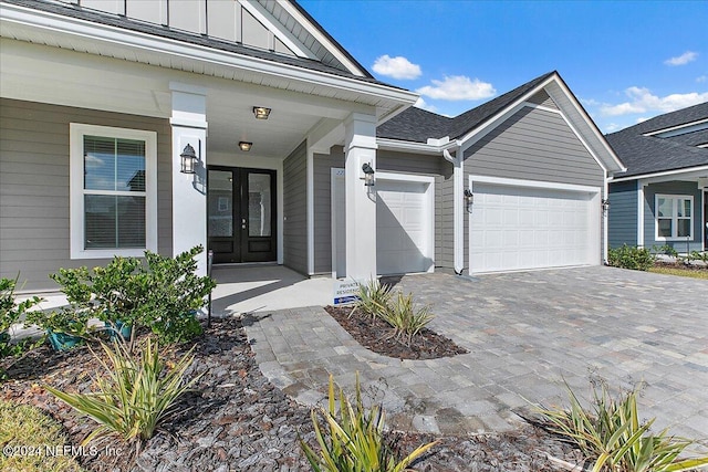 entrance to property featuring french doors, decorative driveway, board and batten siding, and an attached garage