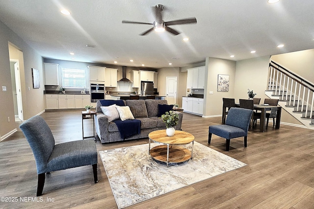 living area with recessed lighting, baseboards, wood finished floors, and stairs