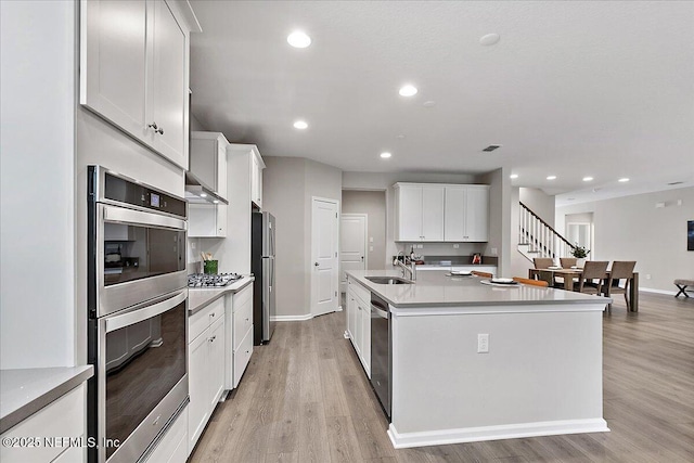 kitchen with light wood finished floors, recessed lighting, appliances with stainless steel finishes, wall chimney exhaust hood, and a sink