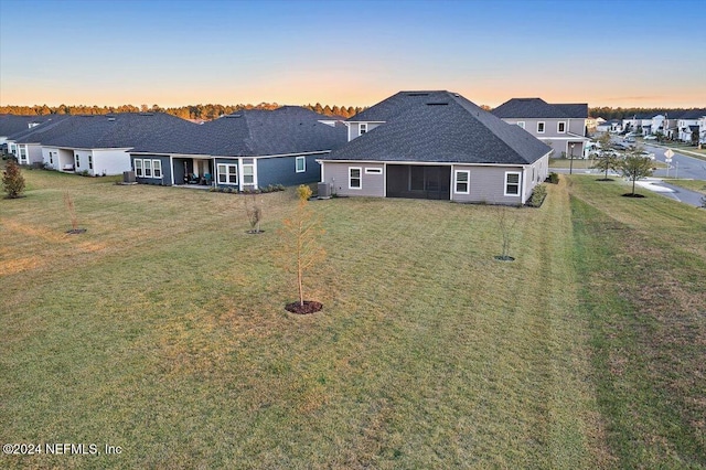 back of property at dusk with a yard, a residential view, and central AC