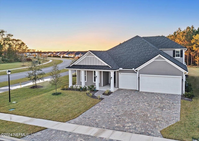 view of front of property featuring a yard, an attached garage, covered porch, decorative driveway, and board and batten siding