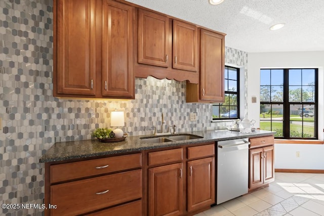 kitchen with dark stone countertops, brown cabinets, a sink, dishwasher, and tasteful backsplash