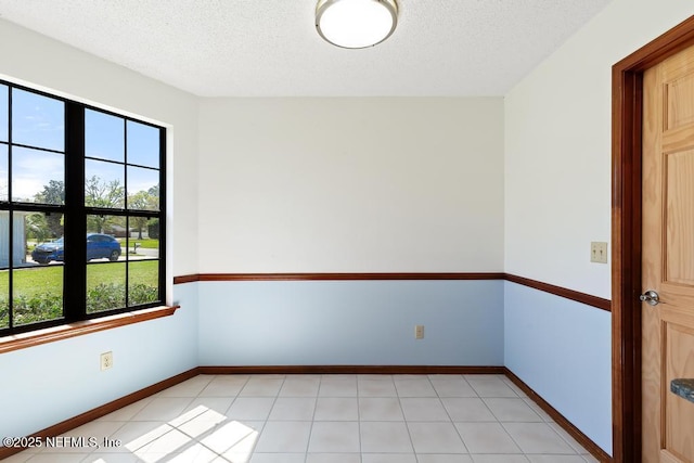 spare room with light tile patterned floors, a textured ceiling, and baseboards