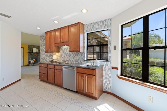 kitchen with visible vents, light tile patterned floors, stainless steel dishwasher, brown cabinetry, and a sink