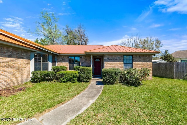 single story home with a front yard, fence, a standing seam roof, brick siding, and metal roof