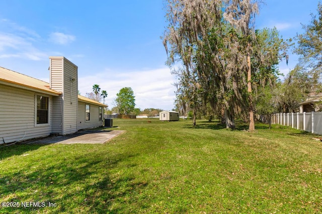 view of yard featuring a storage unit, an outbuilding, a patio, fence, and cooling unit