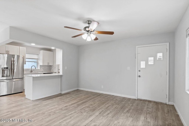 unfurnished living room featuring a ceiling fan, baseboards, light wood-type flooring, and a sink