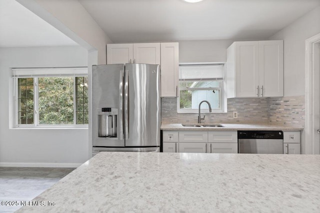 kitchen featuring tasteful backsplash, a wealth of natural light, appliances with stainless steel finishes, white cabinetry, and a sink