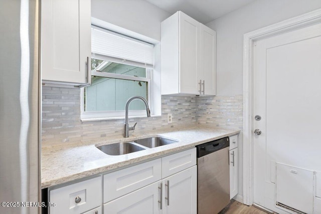 kitchen with tasteful backsplash, light stone countertops, dishwasher, white cabinets, and a sink