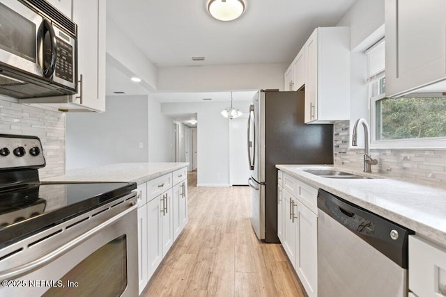 kitchen with light stone countertops, appliances with stainless steel finishes, light wood-style floors, white cabinets, and a sink