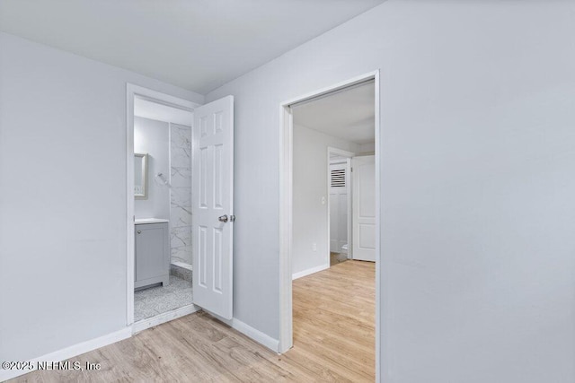 unfurnished bedroom featuring connected bathroom, baseboards, and light wood-style floors