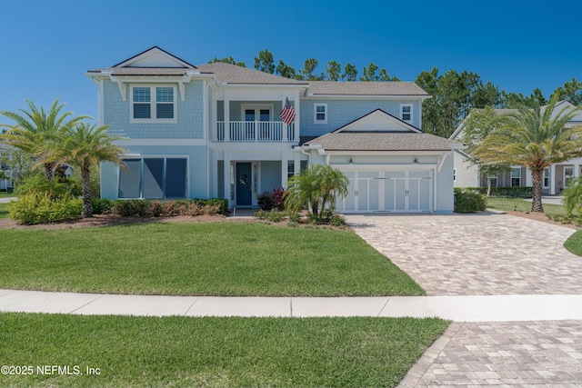 view of front of home featuring decorative driveway, a balcony, an attached garage, and a front yard