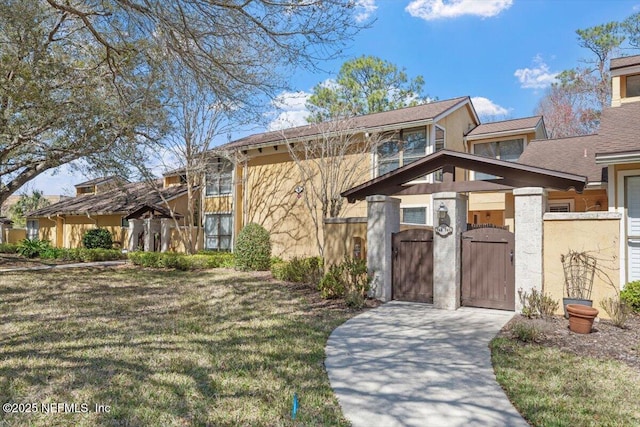 view of front of property featuring stucco siding, a front yard, and a gate