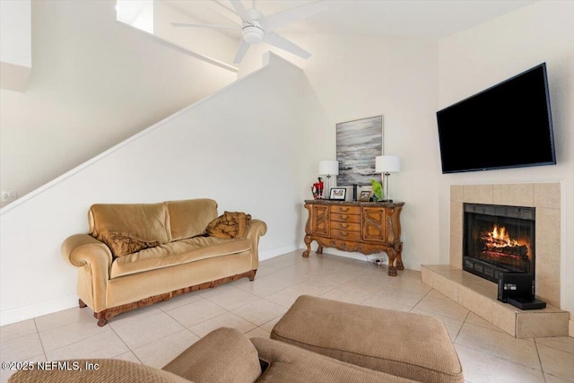 living area featuring tile patterned floors, a tiled fireplace, baseboards, and a ceiling fan