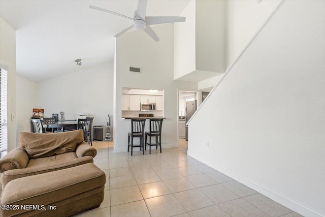 living room featuring a ceiling fan, visible vents, baseboards, high vaulted ceiling, and light tile patterned flooring