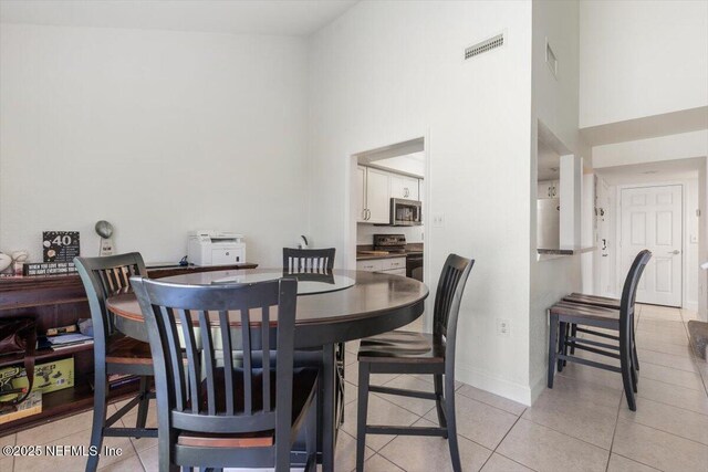 dining room with light tile patterned floors, baseboards, visible vents, and a towering ceiling