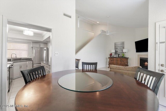 dining room with visible vents, crown molding, a lit fireplace, light tile patterned floors, and a raised ceiling