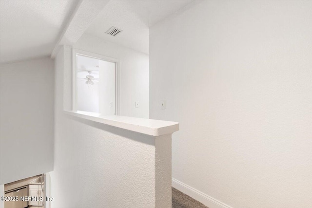 hallway with visible vents, carpet, baseboards, and vaulted ceiling