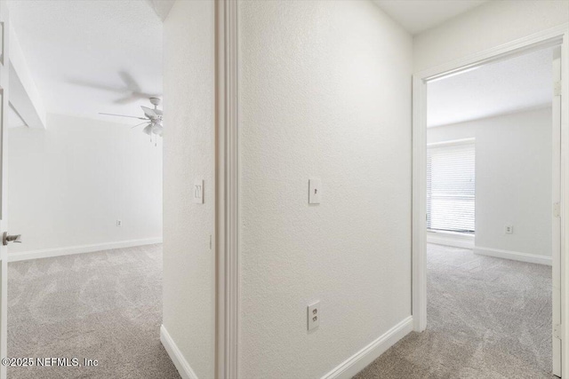 hall with a textured wall, baseboards, and carpet floors