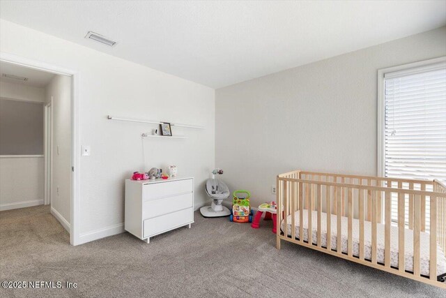 carpeted bedroom featuring visible vents, baseboards, and a nursery area