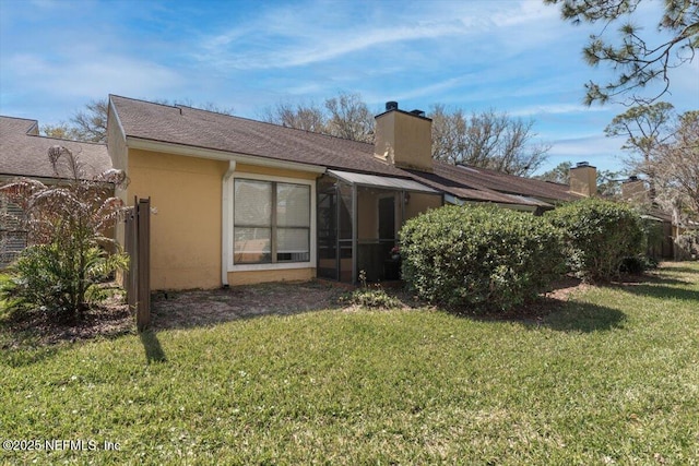 back of property with a lawn, a chimney, a sunroom, and stucco siding