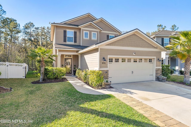 craftsman-style home with a front lawn, fence, driveway, stone siding, and an attached garage