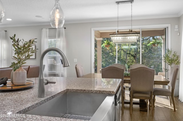 kitchen with crown molding, pendant lighting, wood finished floors, stone countertops, and a sink