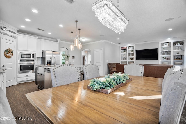 dining space featuring a textured ceiling, dark wood finished floors, arched walkways, an inviting chandelier, and crown molding