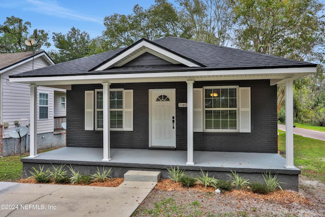 bungalow with brick siding, covered porch, and a shingled roof