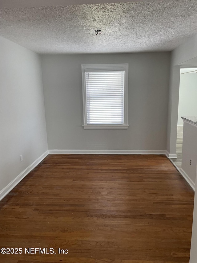 spare room with a textured ceiling, baseboards, and wood finished floors