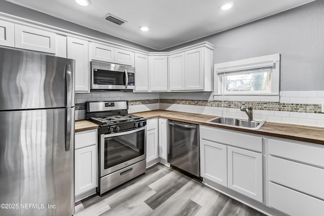 kitchen featuring visible vents, wooden counters, a sink, appliances with stainless steel finishes, and backsplash