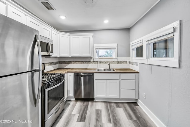 kitchen with visible vents, a sink, white cabinetry, appliances with stainless steel finishes, and butcher block counters