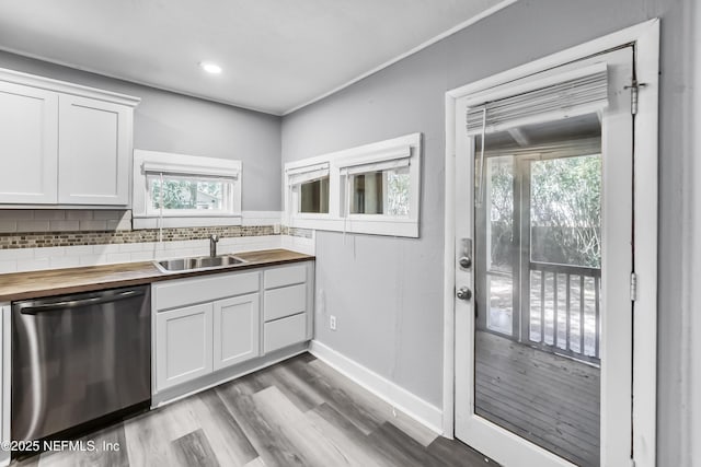 kitchen with wooden counters, a sink, white cabinets, stainless steel dishwasher, and backsplash