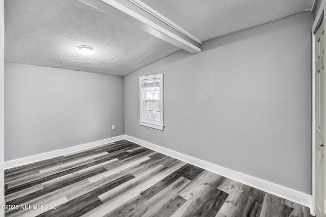 empty room featuring lofted ceiling with beams, baseboards, a textured ceiling, and dark wood-style flooring