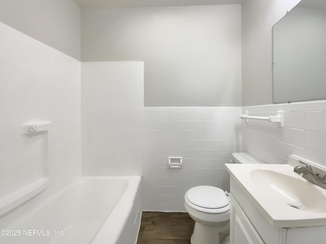 bathroom featuring tile walls, toilet, a bathing tub, wood finished floors, and vanity