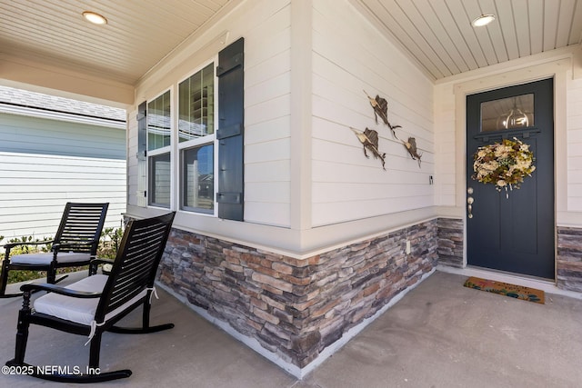 view of exterior entry with stone siding and covered porch