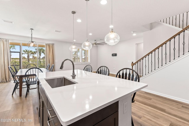 kitchen featuring an island with sink, light countertops, light wood-style floors, and a sink