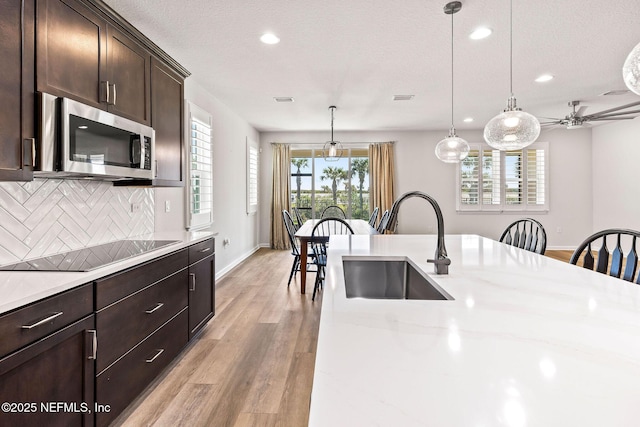 kitchen with stainless steel microwave, decorative light fixtures, light wood-type flooring, black electric cooktop, and a sink