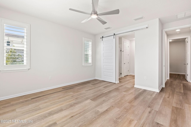 unfurnished bedroom with visible vents, light wood-style flooring, baseboards, and a barn door