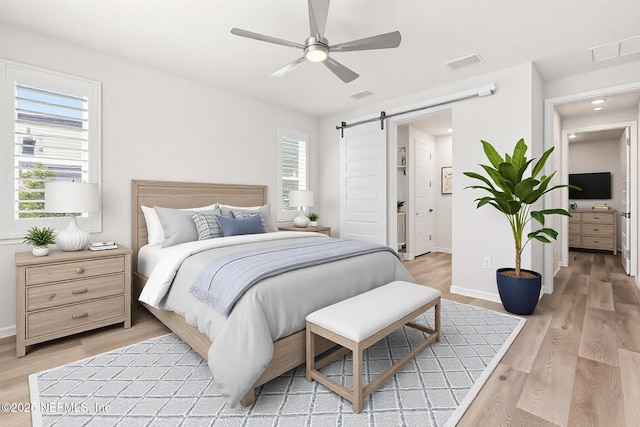 bedroom with visible vents, light wood-style flooring, baseboards, and a barn door