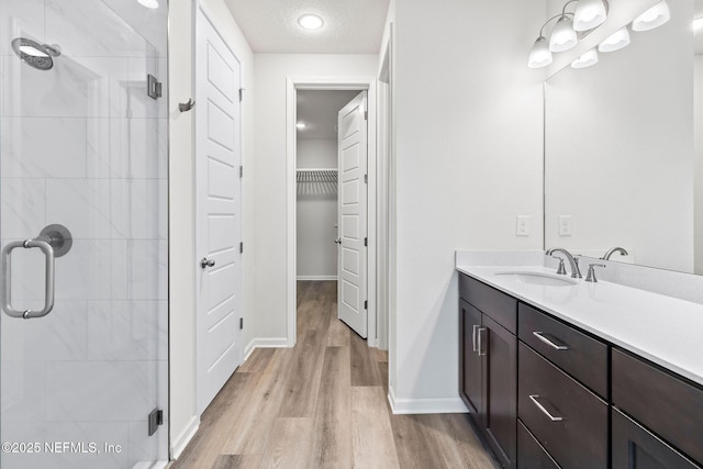 bathroom featuring vanity, wood finished floors, a stall shower, a textured ceiling, and a walk in closet