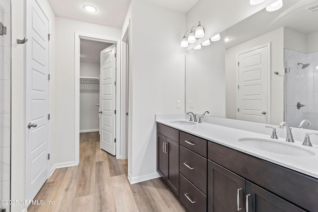 bathroom with wood finished floors, tiled shower, double vanity, and a sink