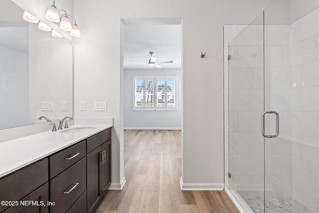 bathroom featuring a stall shower, wood finished floors, baseboards, ceiling fan, and vanity