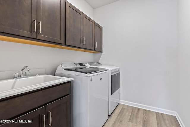 clothes washing area featuring light wood-type flooring, a sink, cabinet space, separate washer and dryer, and baseboards