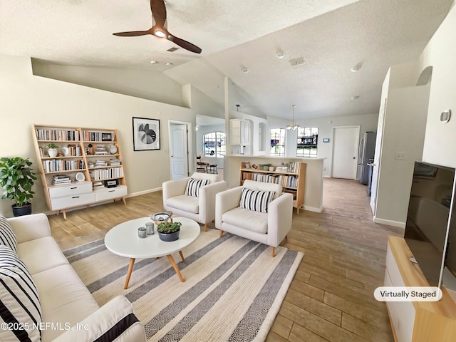 living room with baseboards, light wood-type flooring, lofted ceiling, ceiling fan with notable chandelier, and a textured ceiling